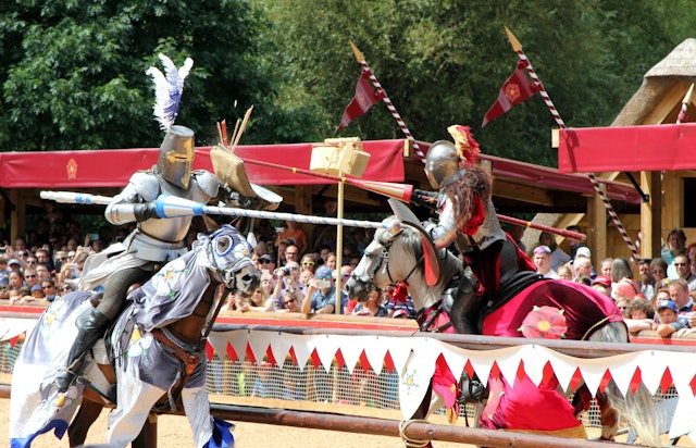Two knights in armour riding horses approach each other with jousting sticks in a battle re-enactment with a crowd of onlookers