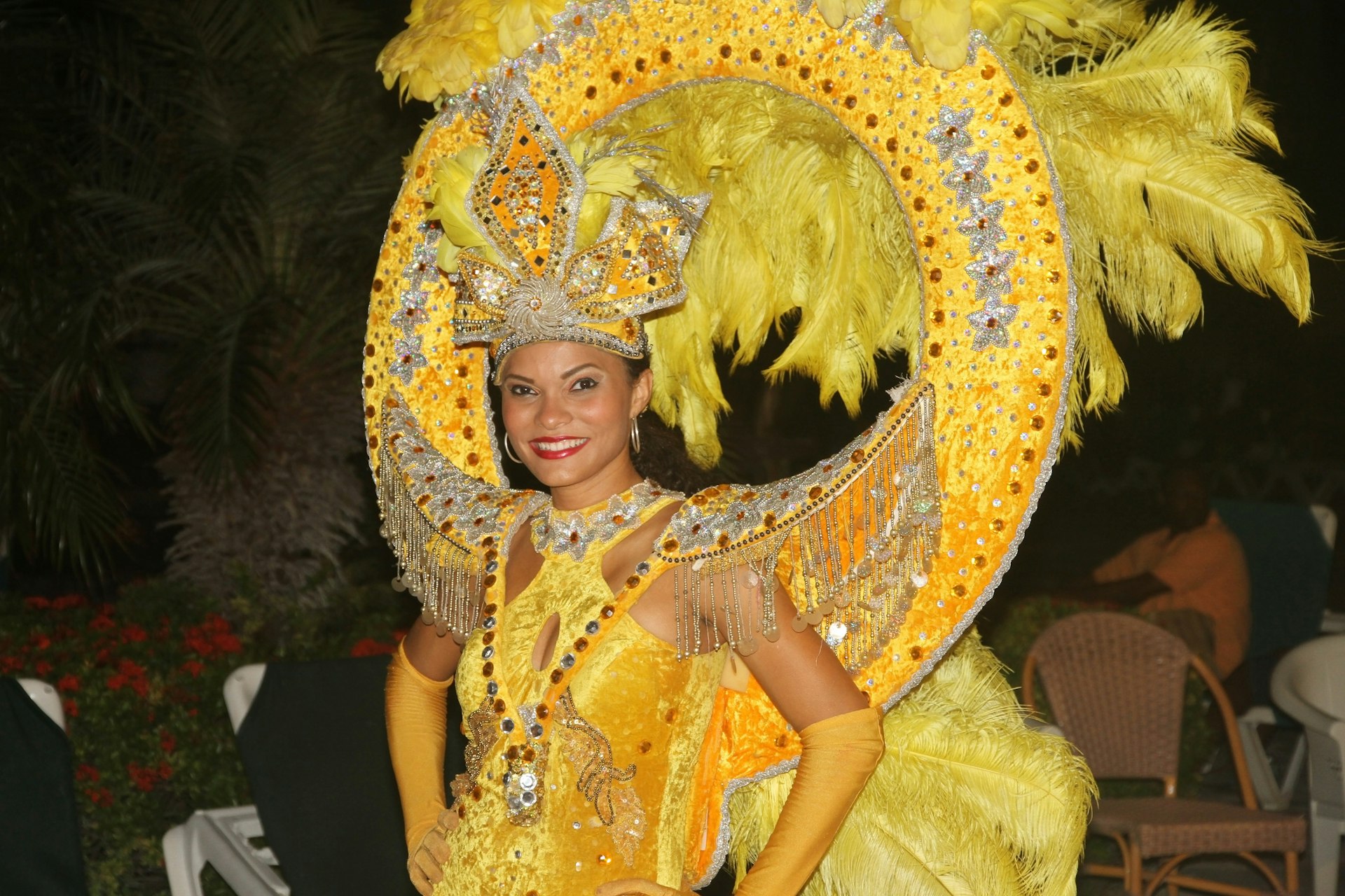 A woman wears a golden sparkling costume with a large head piece as she performs a traditional Aruban dance.