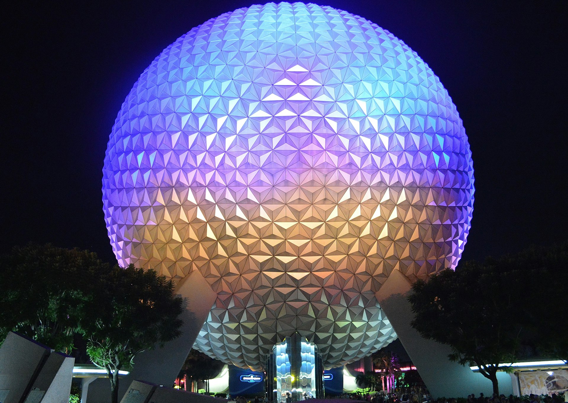 A large silver-grey sphere is lit up with purple and gold lights against the night sky