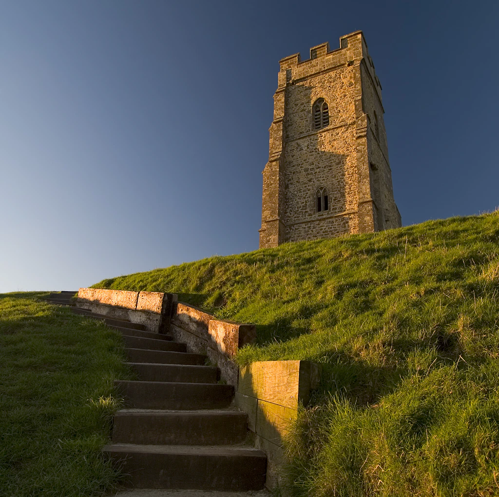 Glastonbury Tor, Somerset Steps in a steep grassy hillside. A large church-like tower stands at the top of the hill.