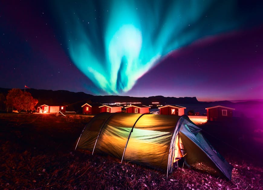 A vibrant green Aurora Borealis above several tents glowing with light inside