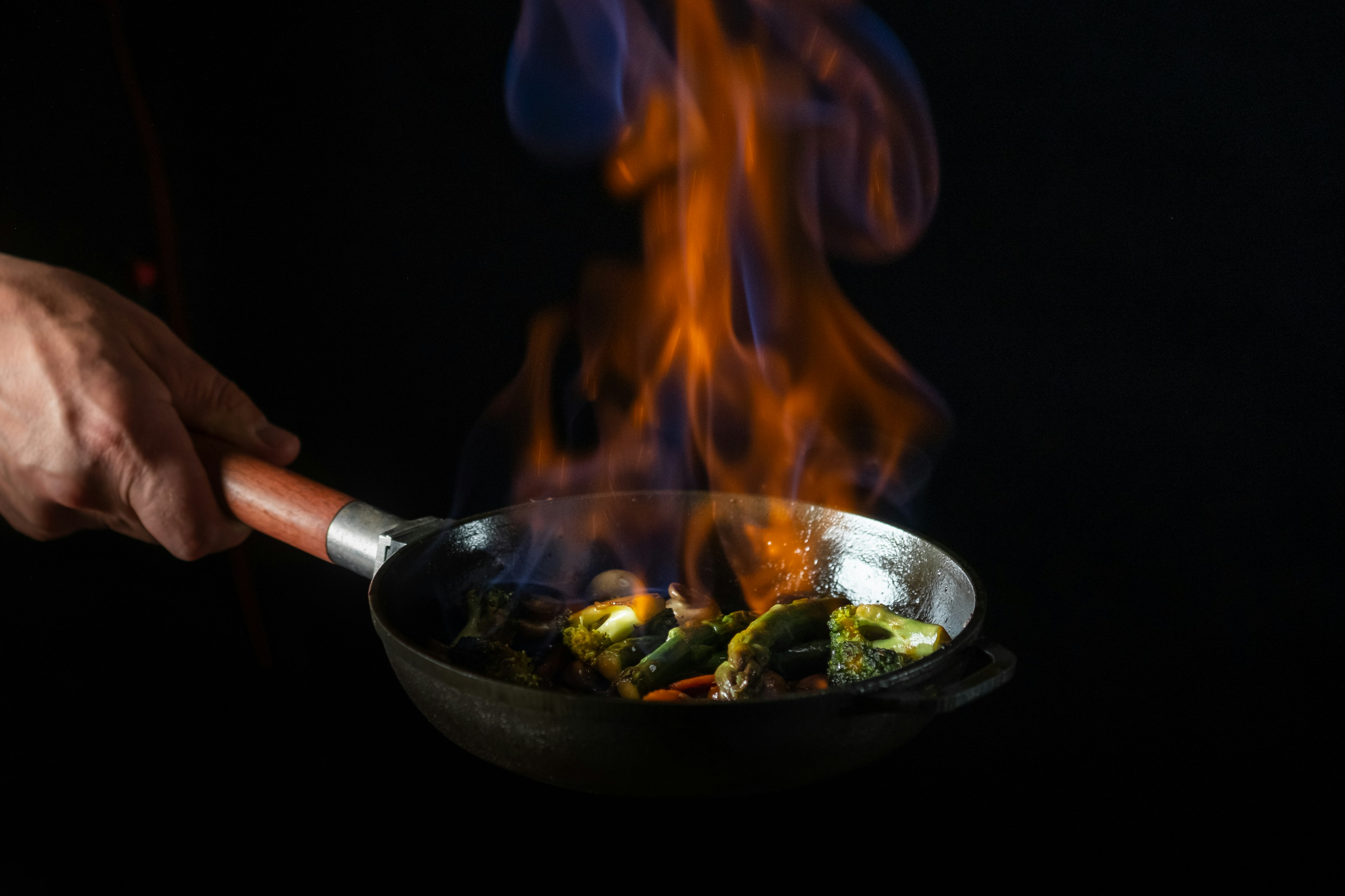 厨师在锅中用火焰在黑色背景上烹饪食物。餐厅和酒店服务概念。