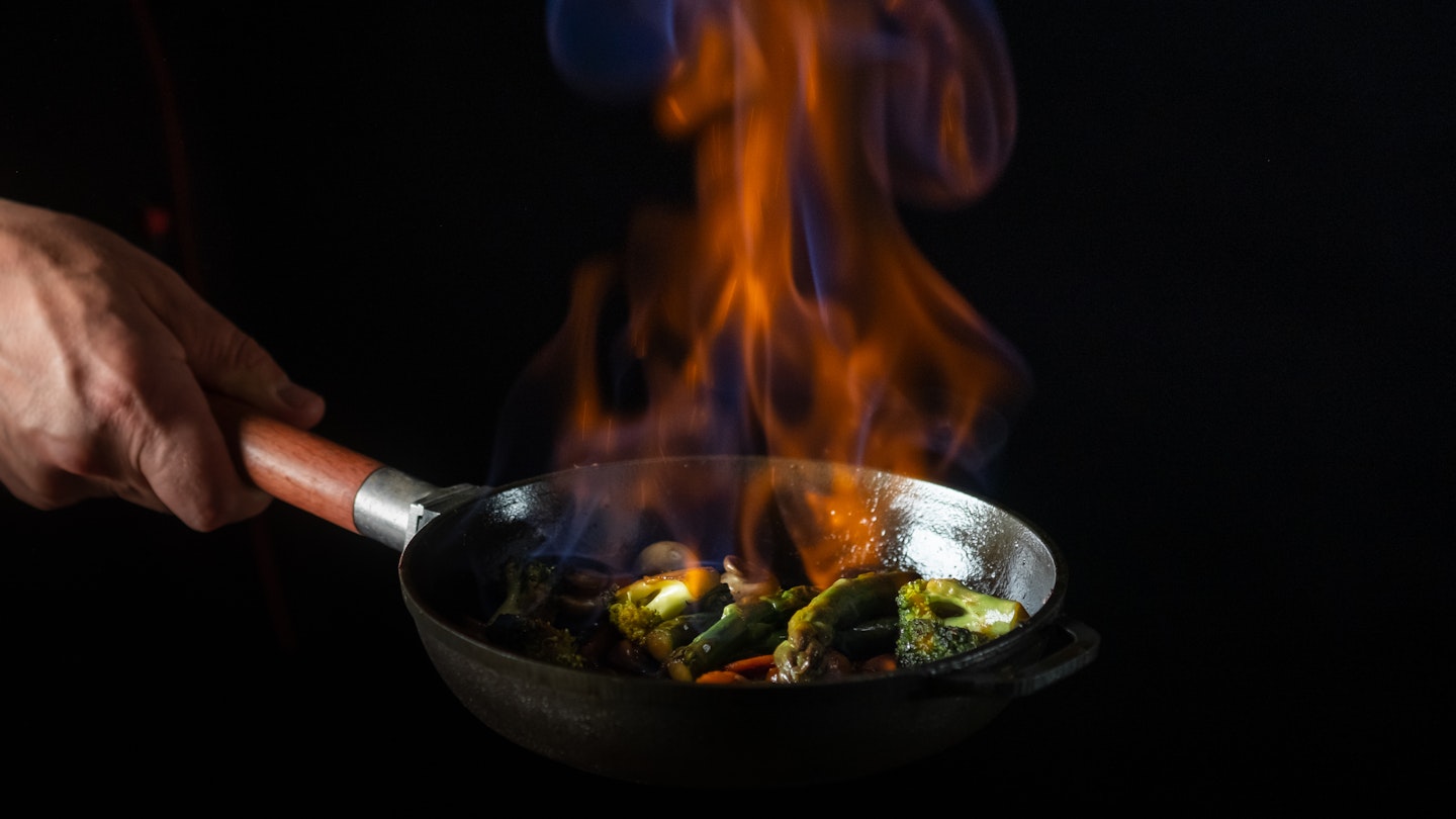 Chef cooking food in pan with fire flame on black background. Restaurant and hotel service concept.