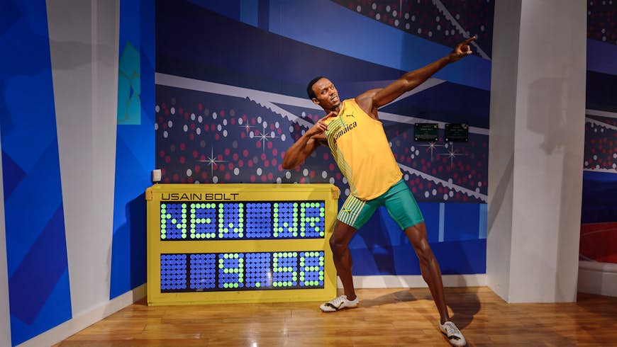 Jamaican athlete Usain Bolt stands in his trademark pose with arms pointing at an angle upwards as he leans, standing next to his world record 100m time of 9.58 seconds
