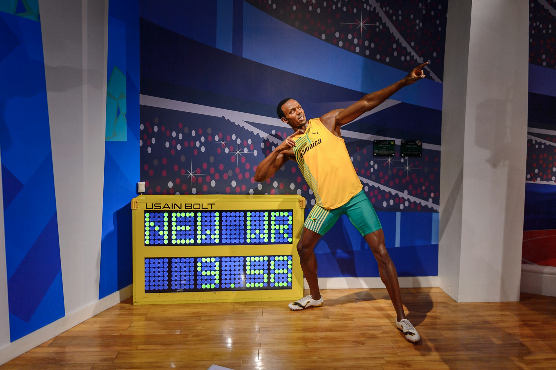 Jamaican athlete Usain Bolt stands in his trademark pose with arms pointing at an angle upwards as he leans, standing next to his world record 100m time of 9.58 seconds