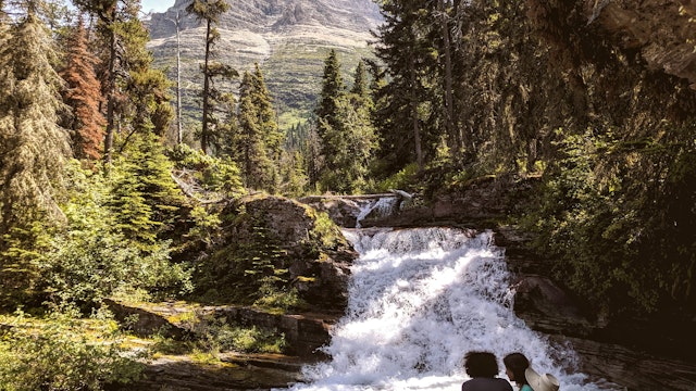 A couple sits by No Name Falls in Glacier National Park
