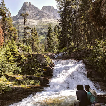A couple sits by No Name Falls in Glacier National Park