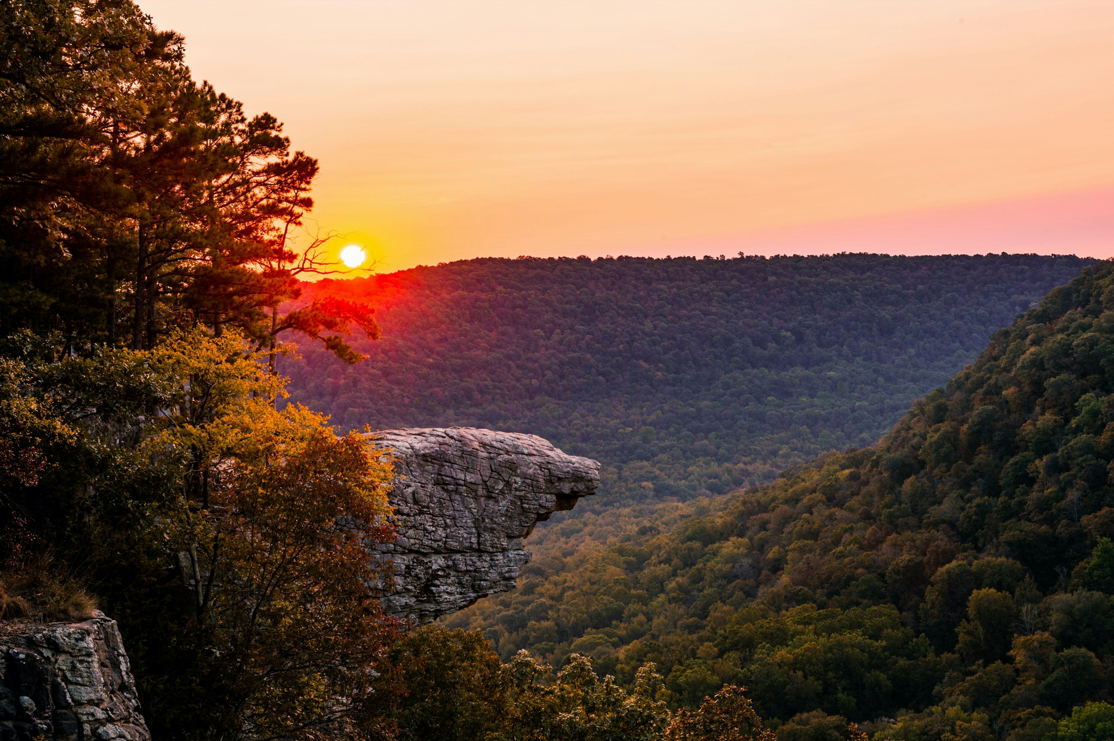 The sun rises over Whitaker Point, known as Hawksbill Crag, in Arkansas as the fall colors begin to set in on the trees