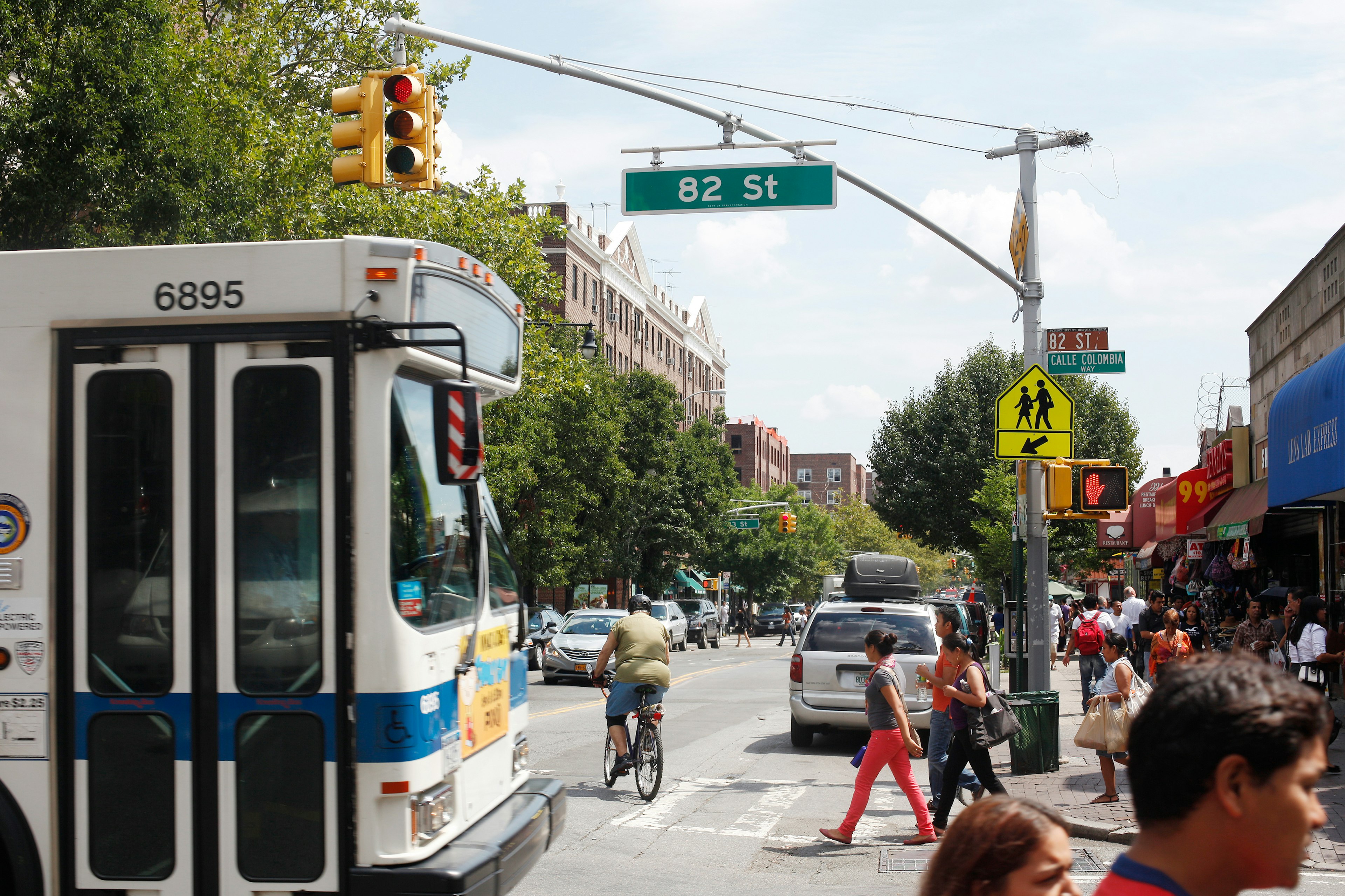 A New York City bus at an intersection in Queens, with people crossing in front