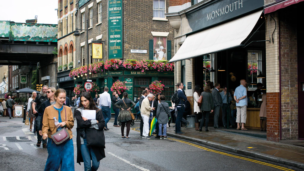 Borough Market, London People walk along in the street beside a large food market. The street is lined with pubs and cafes