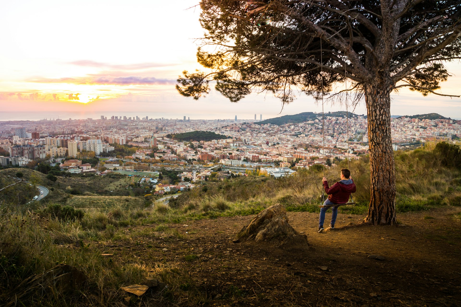 Guy enjoying sunrise over Barcelona city from the tree swing in Collserola