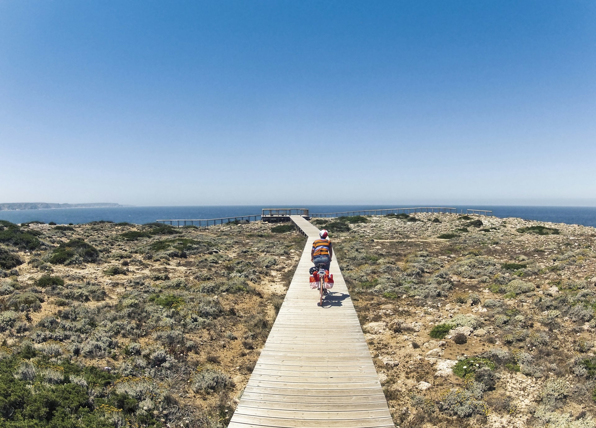 Young woman riding bicycle on wooden walkway at coast, Carrapateira, Algarve, Portugal