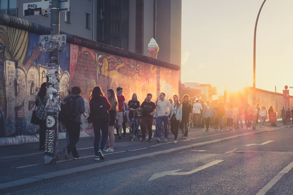 Young people walk beside the East Side Gallery on a summer evening with the sun setting in the background.