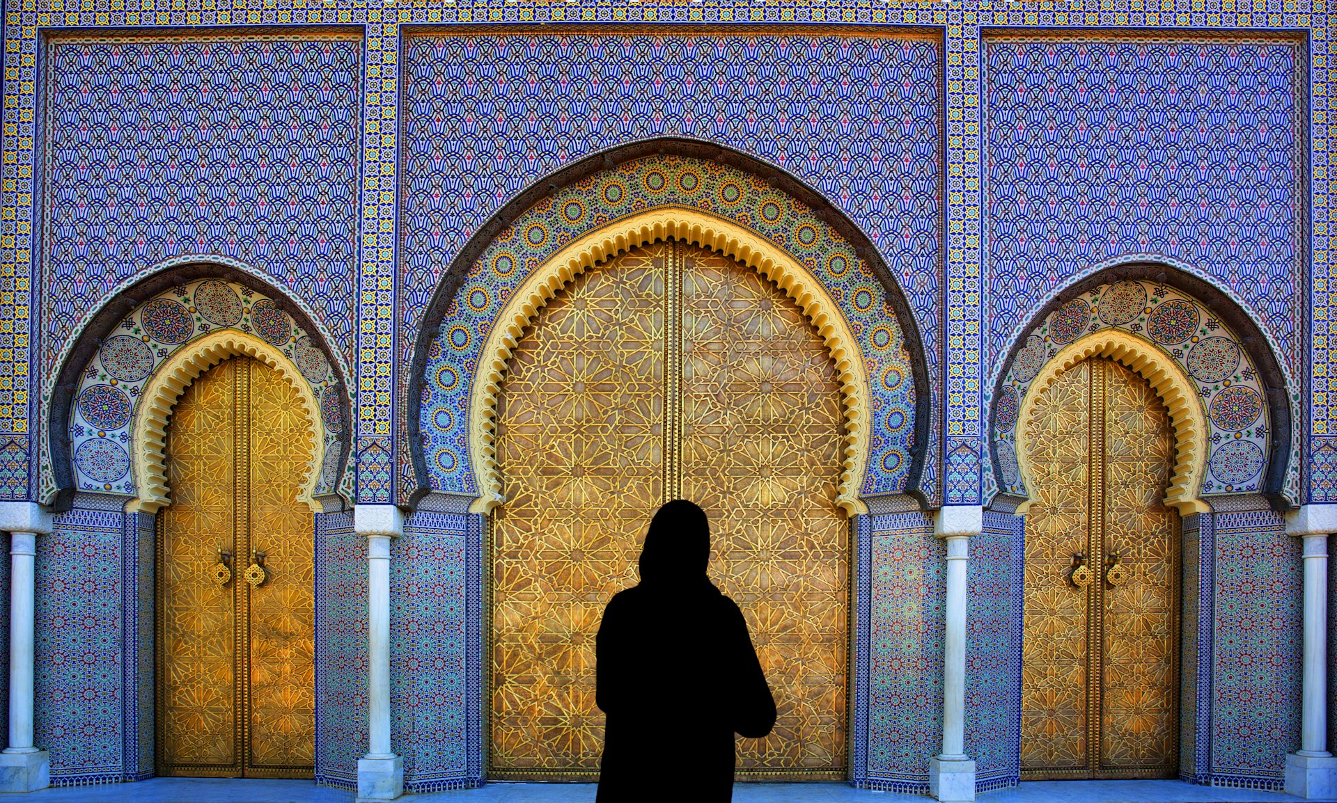 A woman in black stands in front of ornately decorated doors in Fez, Morocco