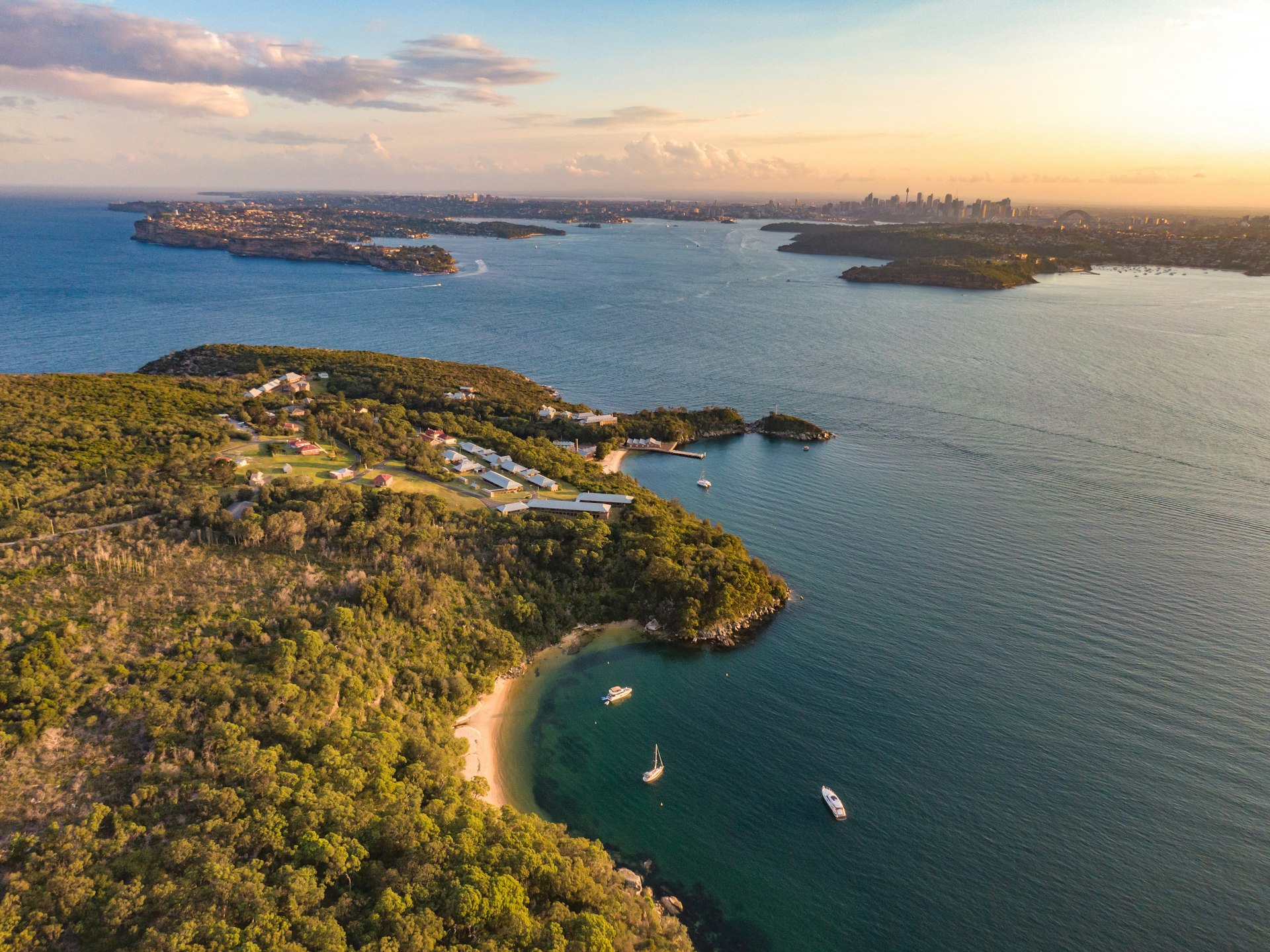 Aerial drone evening view of the Quarantine Station, part of Sydney Harbour National Park. Store Beach in foreground. Sydney harbour with North Head & South Head and city skyline in background.