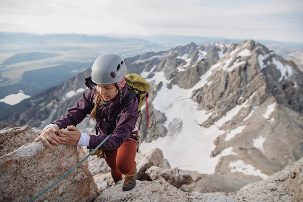 Female rock climber wearing helmet climbs a cliff in the Tetons
