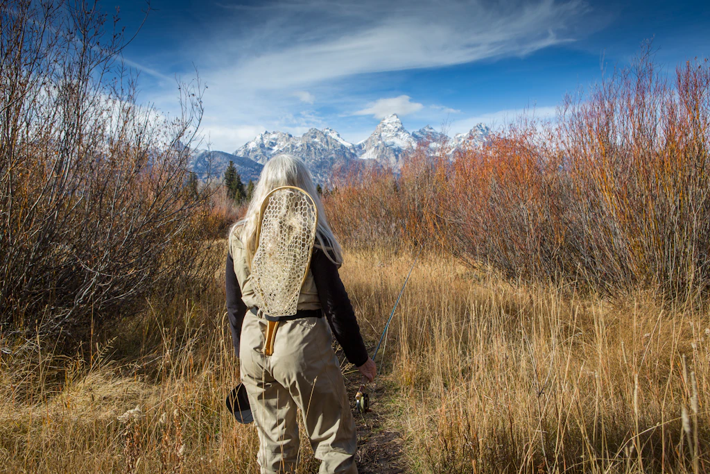 Older Caucasian woman carrying fishing supplies in field