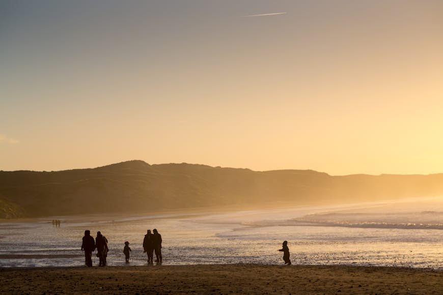 Four adults and two small people are silhouetted at sunset while walking on the beach