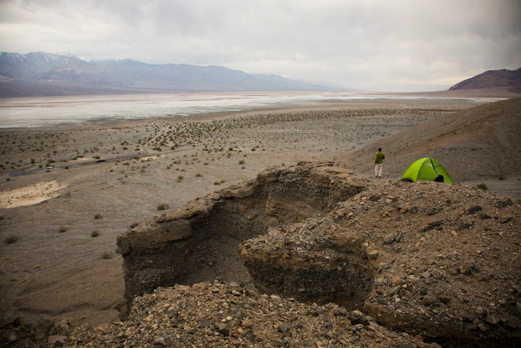A man stands near his green tent overlooking Death Valley National Park,CA.