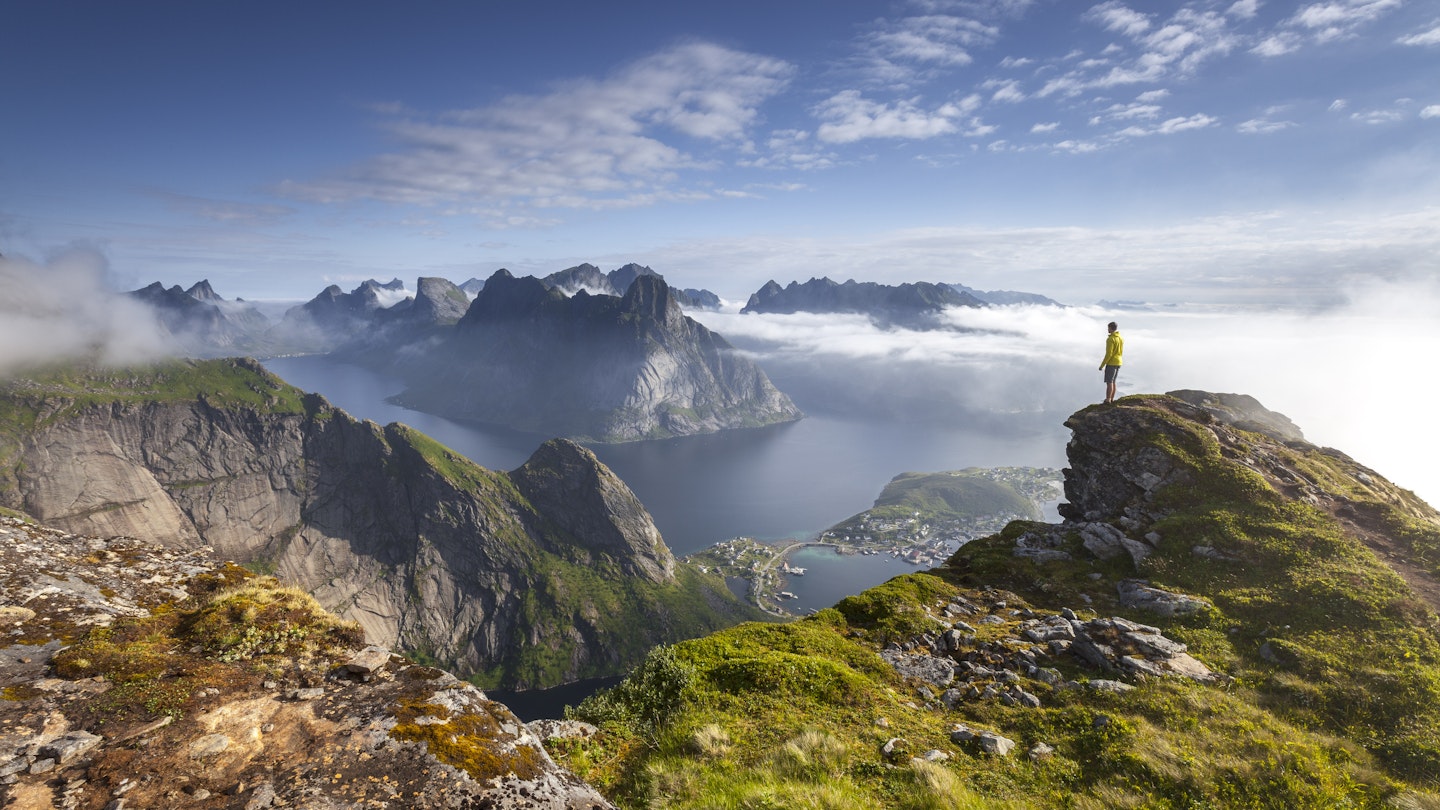 Man stands on the end of a rocky outcrop in Lofoten during sunrise.