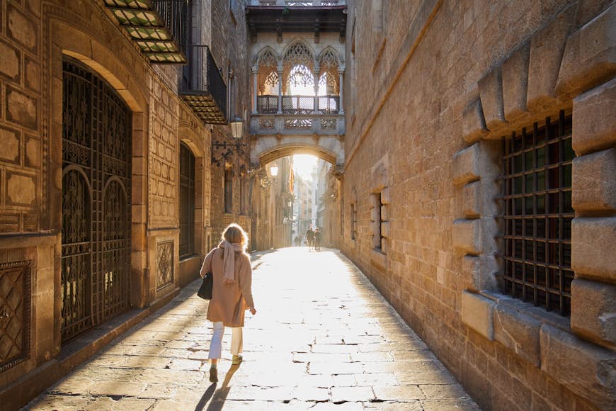 A woman walks through an otherwise empty, sunlit street in the Gothic Quarter of Barcelona