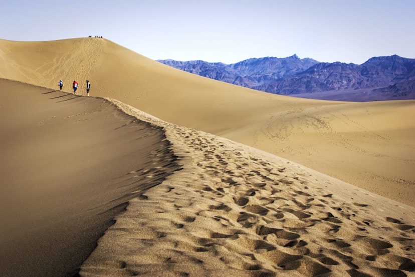 People walking on Mesquite dunes with footprints in Death Valley National Park.