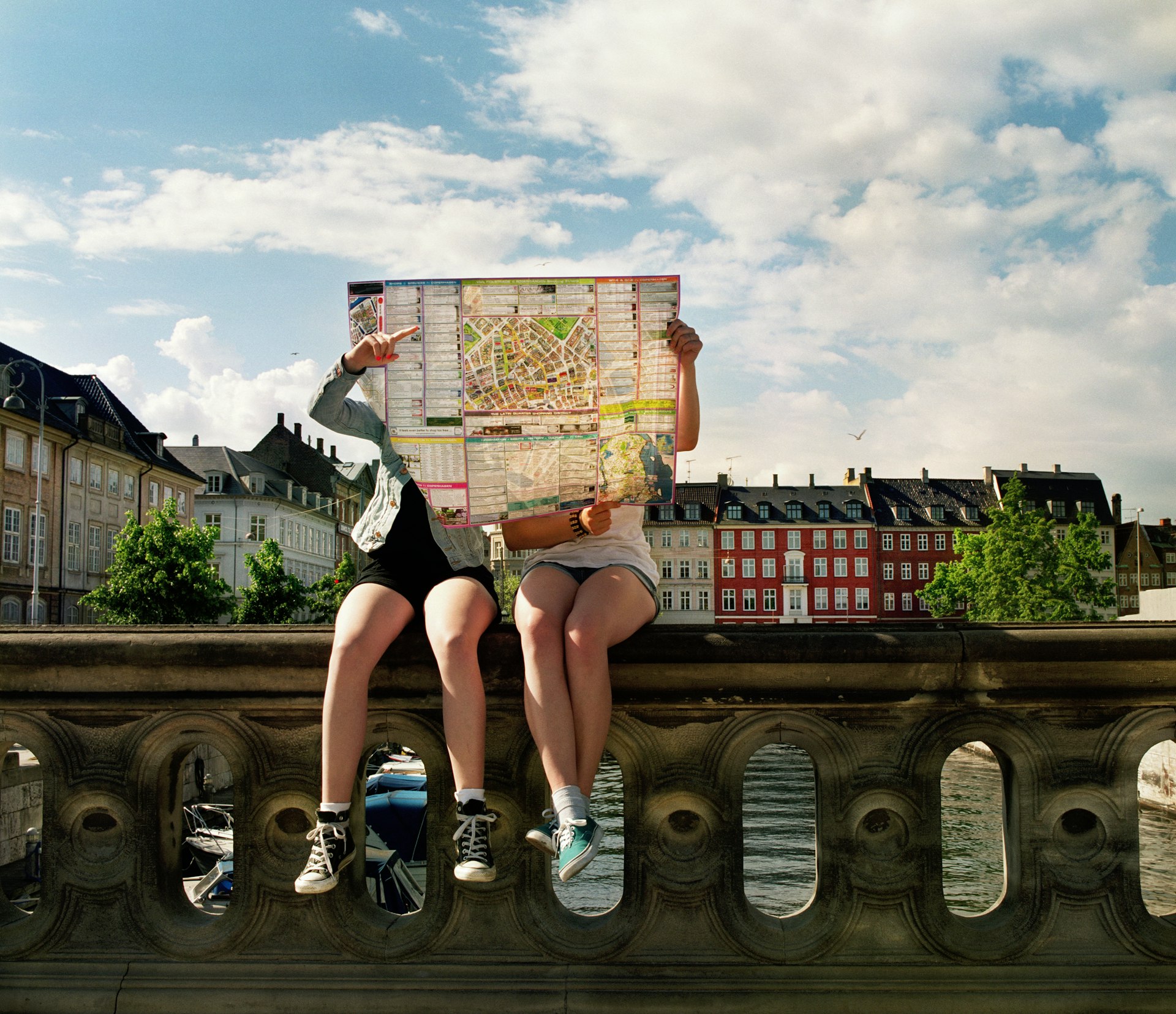 Two teenage girls sitting on bridge holding city map in front of them