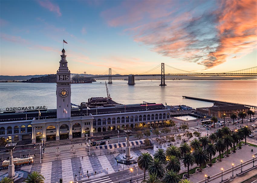 The Ferry Building in San Francisco with its elevated clock tower and the East Bay in the background at sunrise.