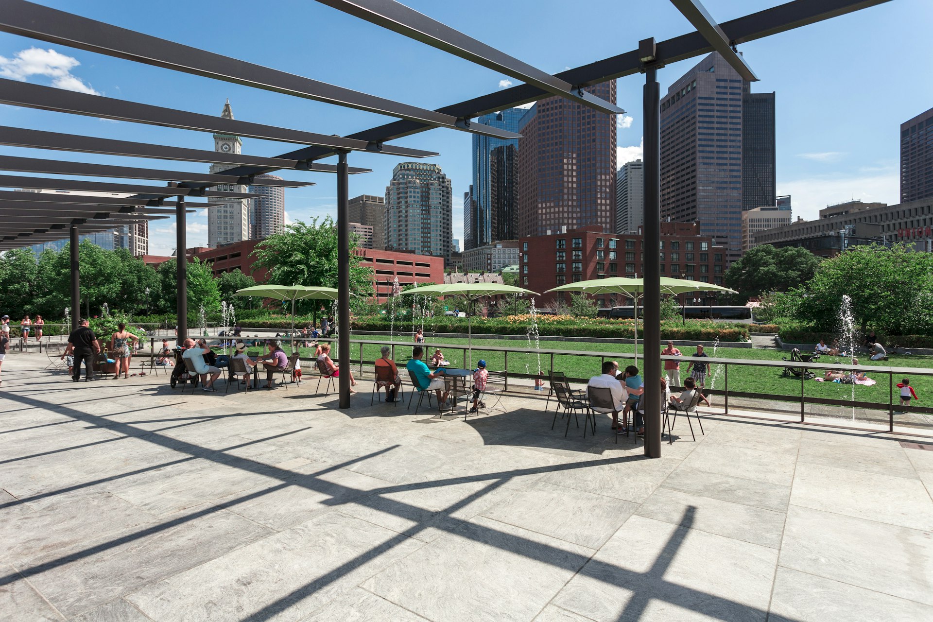 People sitting at tables under umbrellas at the Rose Fitzgerald Kennedy Greenway's North End Park 