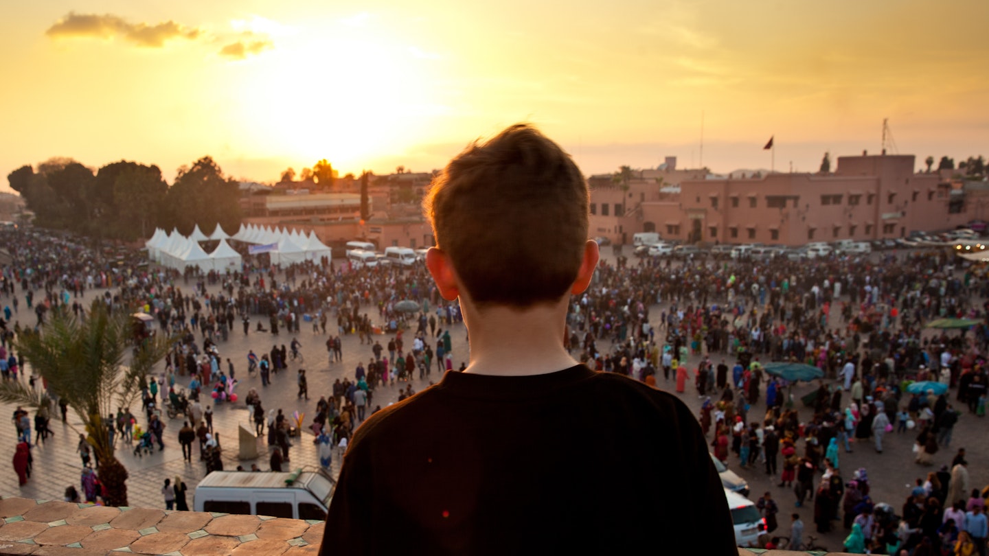 Boy looking out onto Jemaa el Fna square in Marrakech, Morocco at sunset.