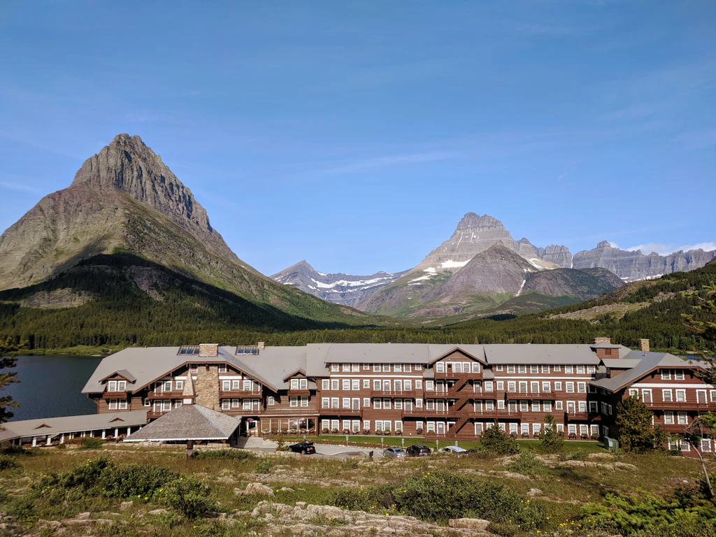 IMG_20190707_085827.jpg A classic alpine lodge sits by a bright blue lake under towering, jagged grey mountain peaks