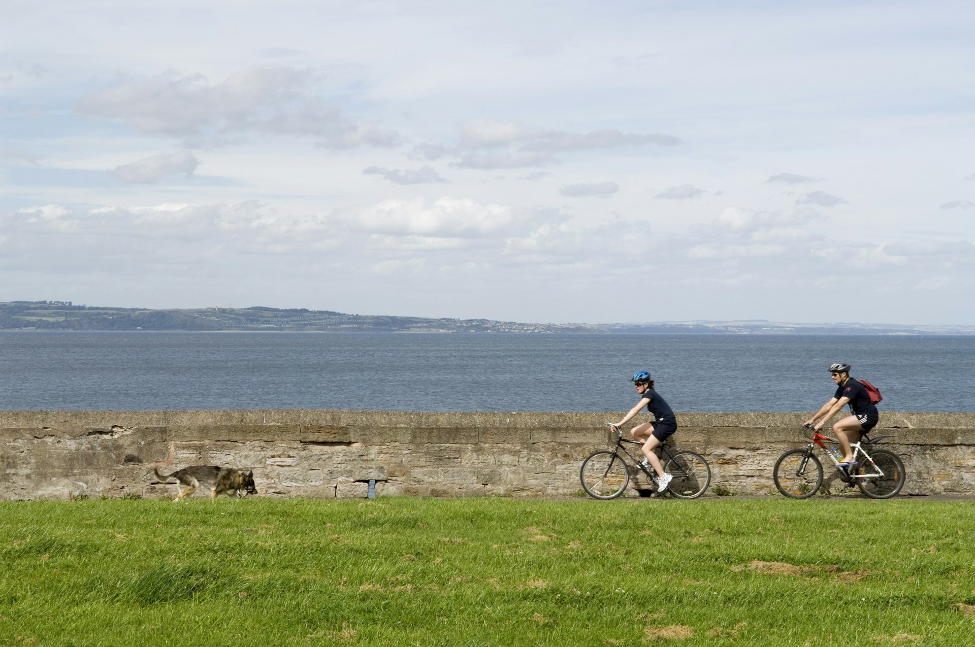 Two cyclists ride their bikes along a path near a body of water
