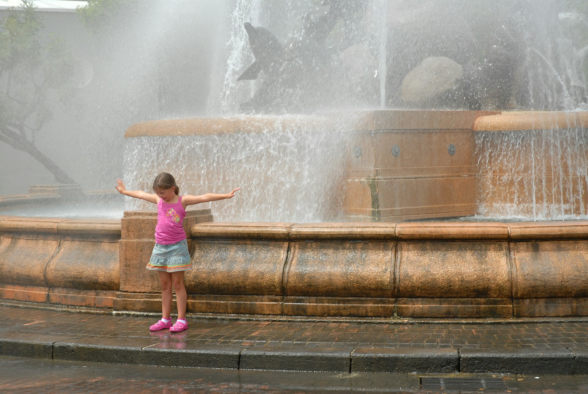 A young girl cooling off in the fountain mist 