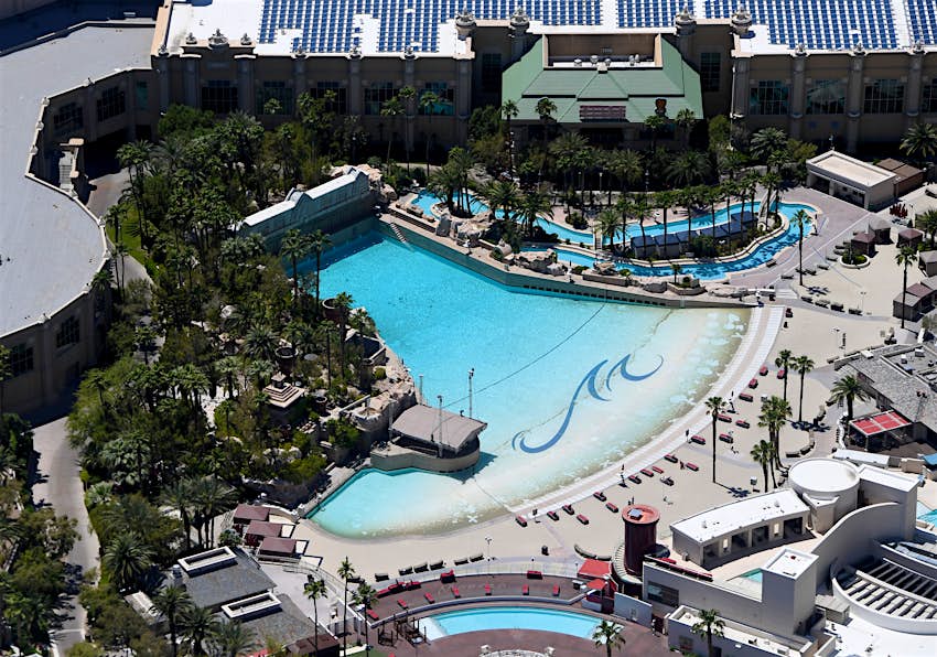 Aerial view of Mandalay Bay's man-made beach, which is a large fan-shaped pool.  It's surrounded by palm trees and poolside cabanas.  The rear of Mandalay Bay can also be seen. 