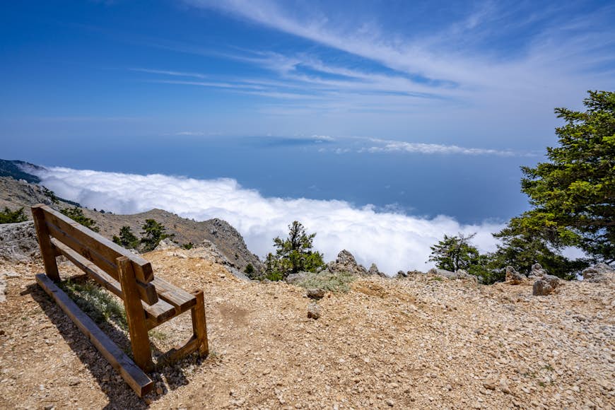 A wooden bench on the summit of Mount Ainos, Kefalonia. The view looks down over the island, which is shrouded in cloud. The mountain top is above the cloud line.