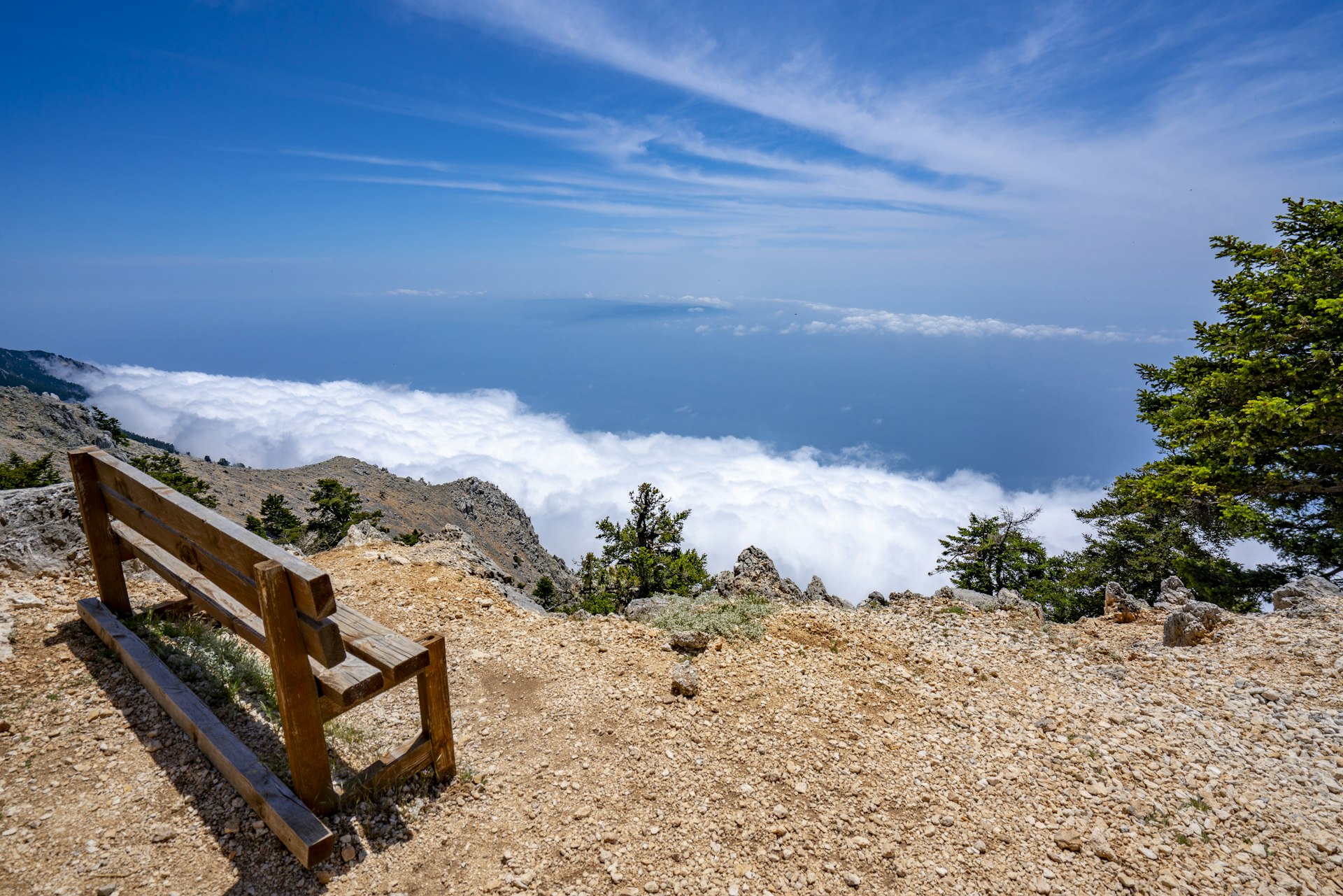 A wooden bench on the summit of Mount Ainos, Kefalonia. The view looks down over the island, which is shrouded in cloud. The mountain top is above the cloud line.