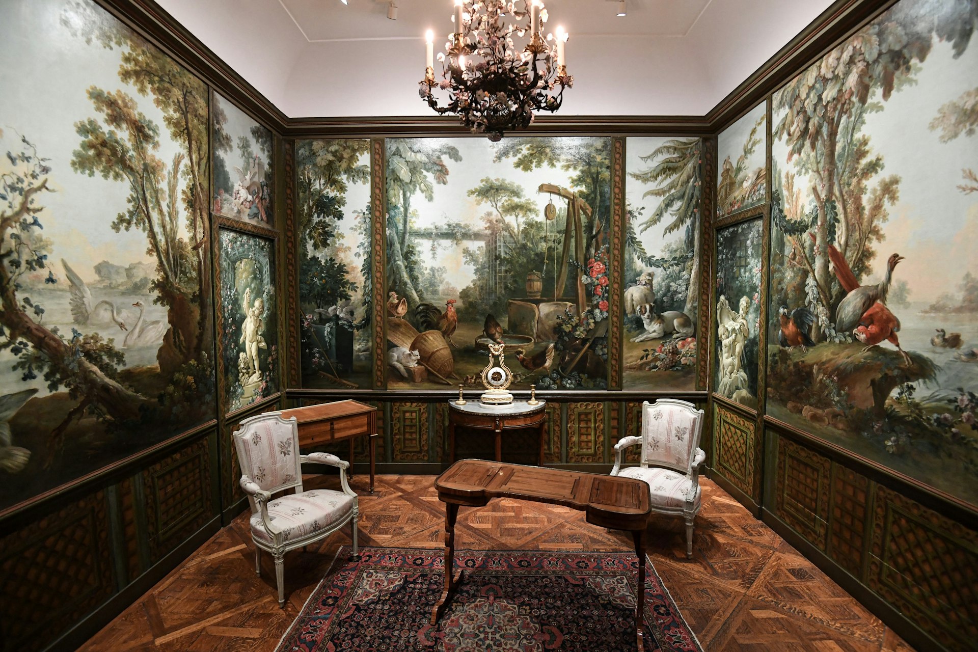 A room with walls painted with murals of woodland and birds, with an ornate table and two chairs in the center 
