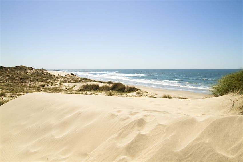 Duna de areia Uma grande duna de areia. Além disso, a extensão plana da praia arenosa é visível e as ondas quebram em direção à costa.