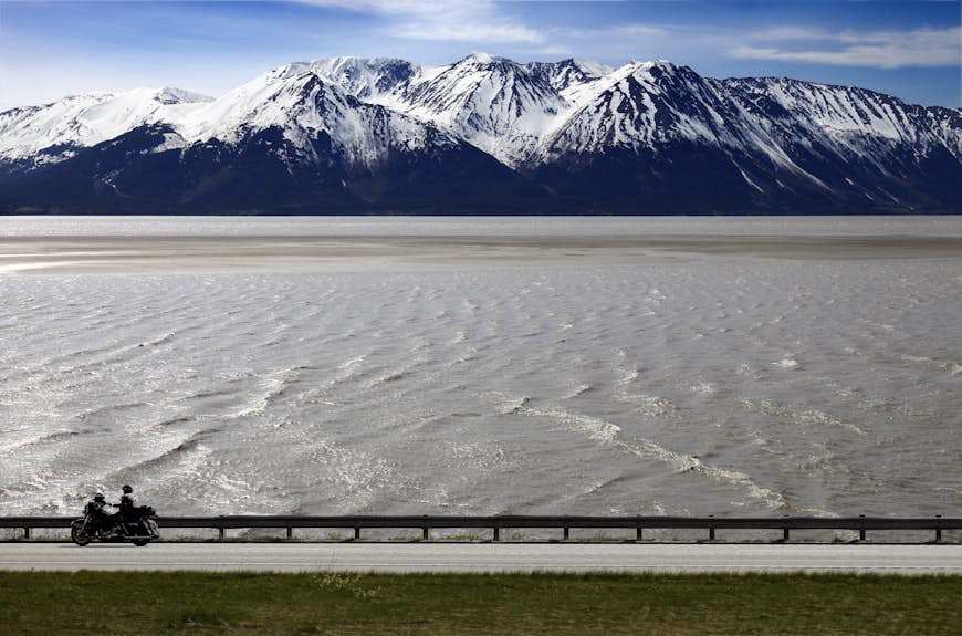 A person on a motorcycle drives by the water of Turnagain Arm on a road trip in Alaska