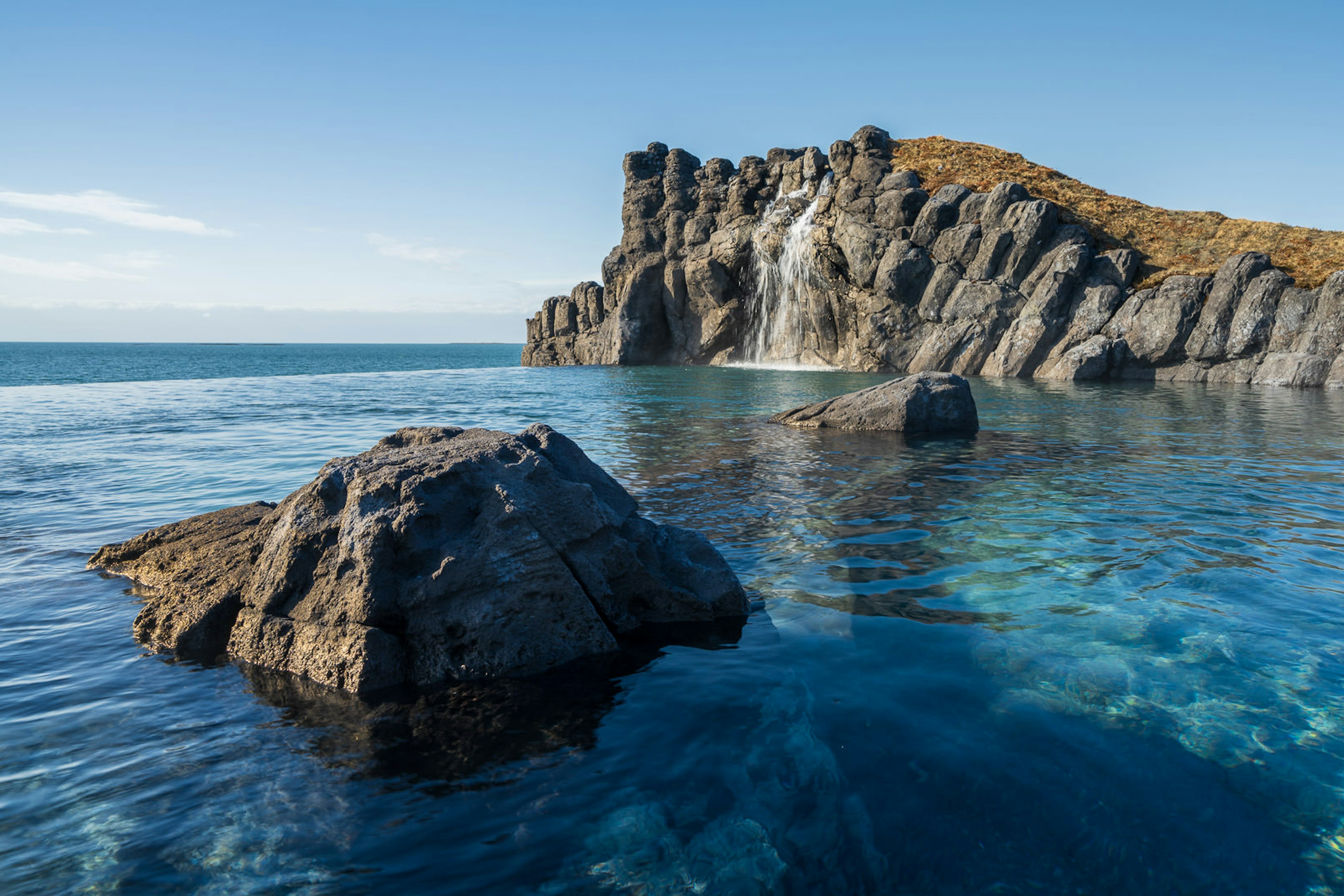 An infinity pool on the side of the ocean with natural rocks.