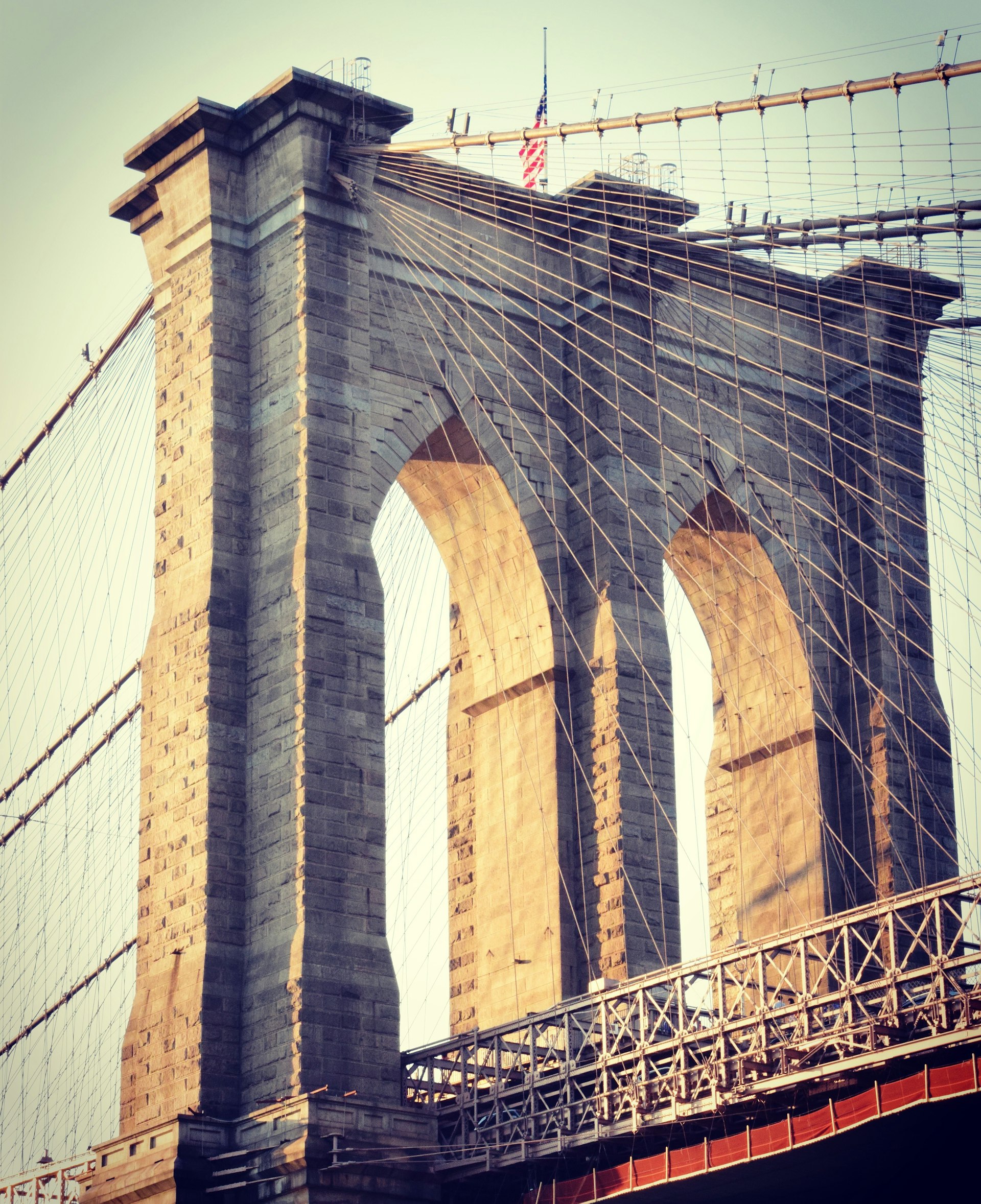 A shot of Brooklyn Bridge from below. Golden light shines through it.