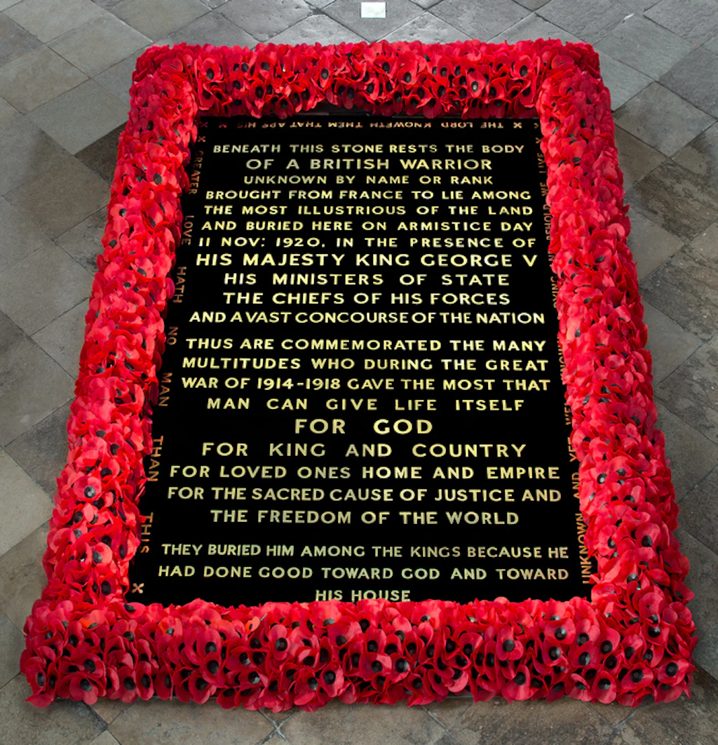 A black gravestone with gold writing surrounded by red poppies marking the Grave of the Unknown Warrior