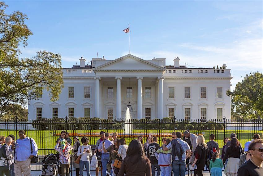 Tourists in front of the White House Tourists stand outside the metal gate taking photos of the White House and the fountain in front of the house.