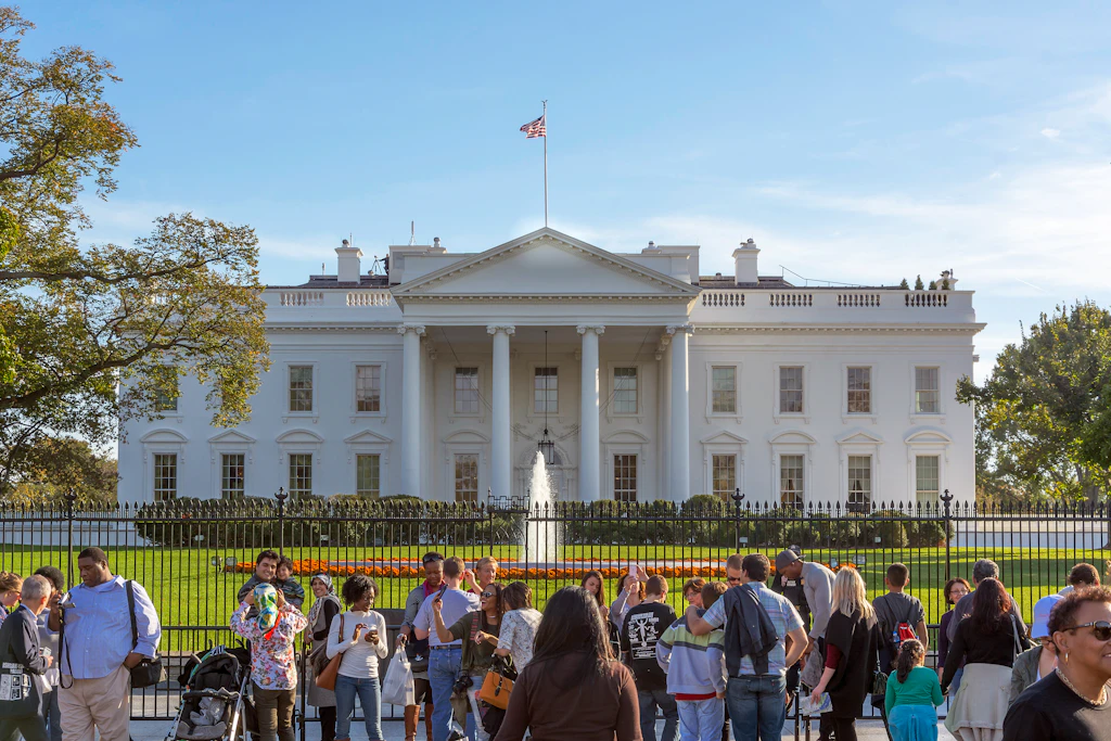 Tourists in front of the White House Tourists stand outside the metal gate taking photos of the White House and the fountain in front of the house.
