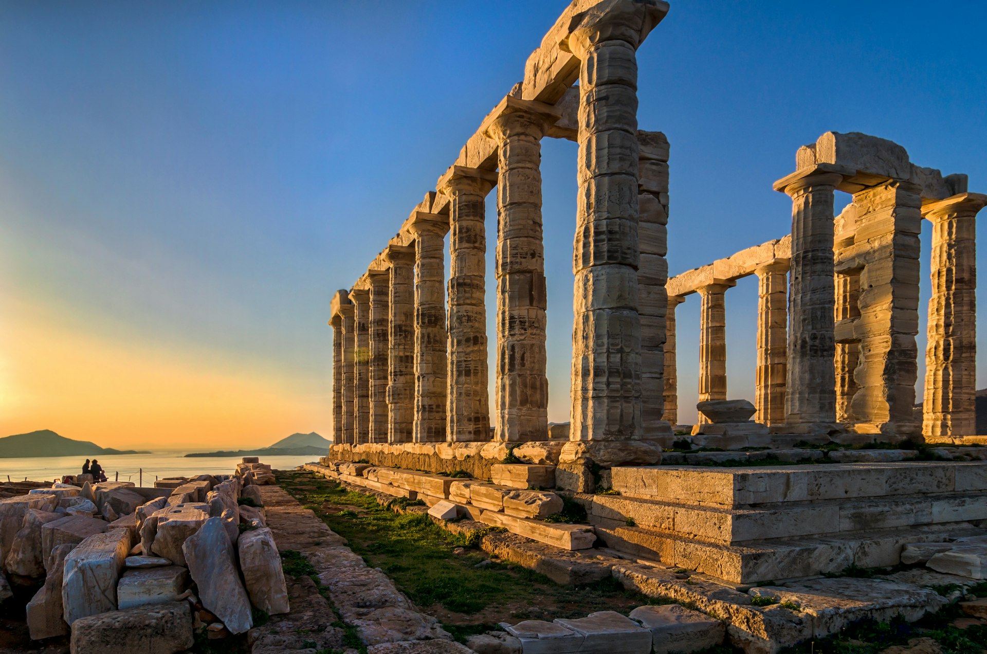 The Temple of Poseidon at cape Sounion during sunset. The ancient temple has a number of white columns and is built on a hilltop overlooking the sea in Greece.