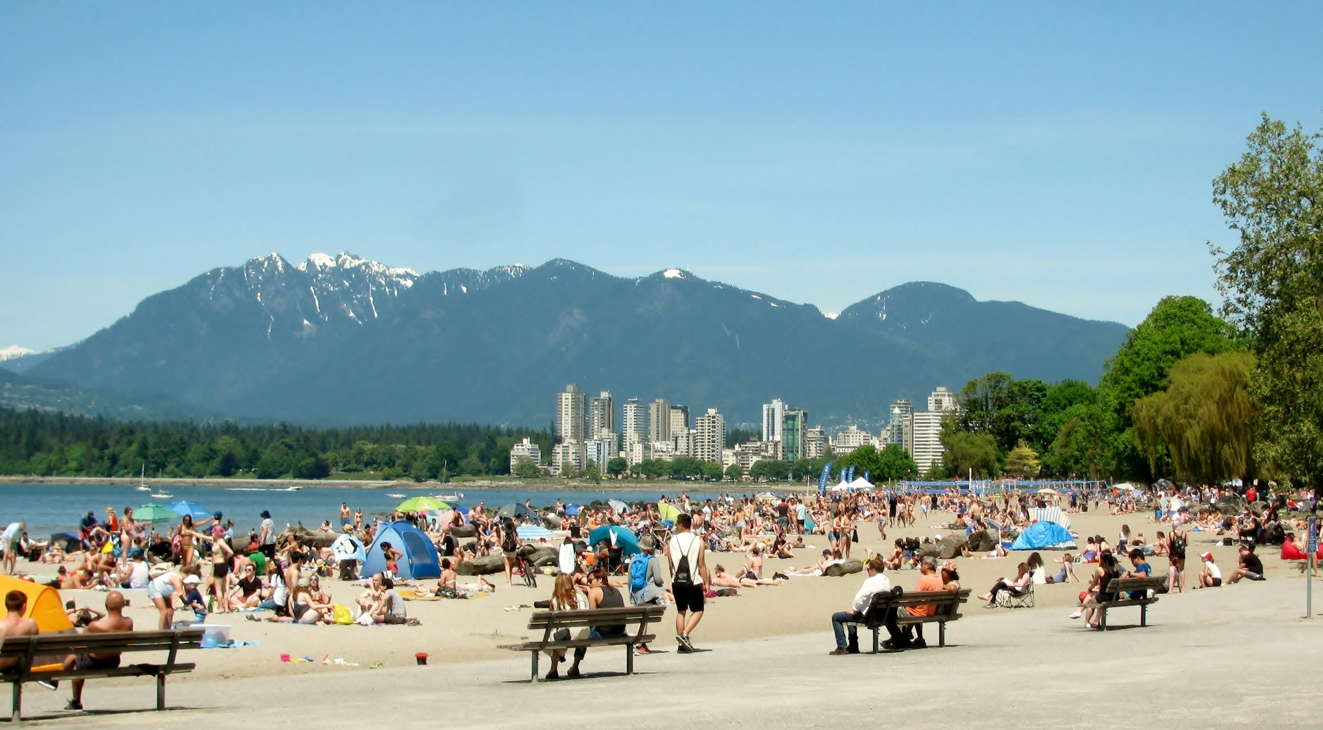 Groups of people relax on the beach with a city skyline and mountains in the distance