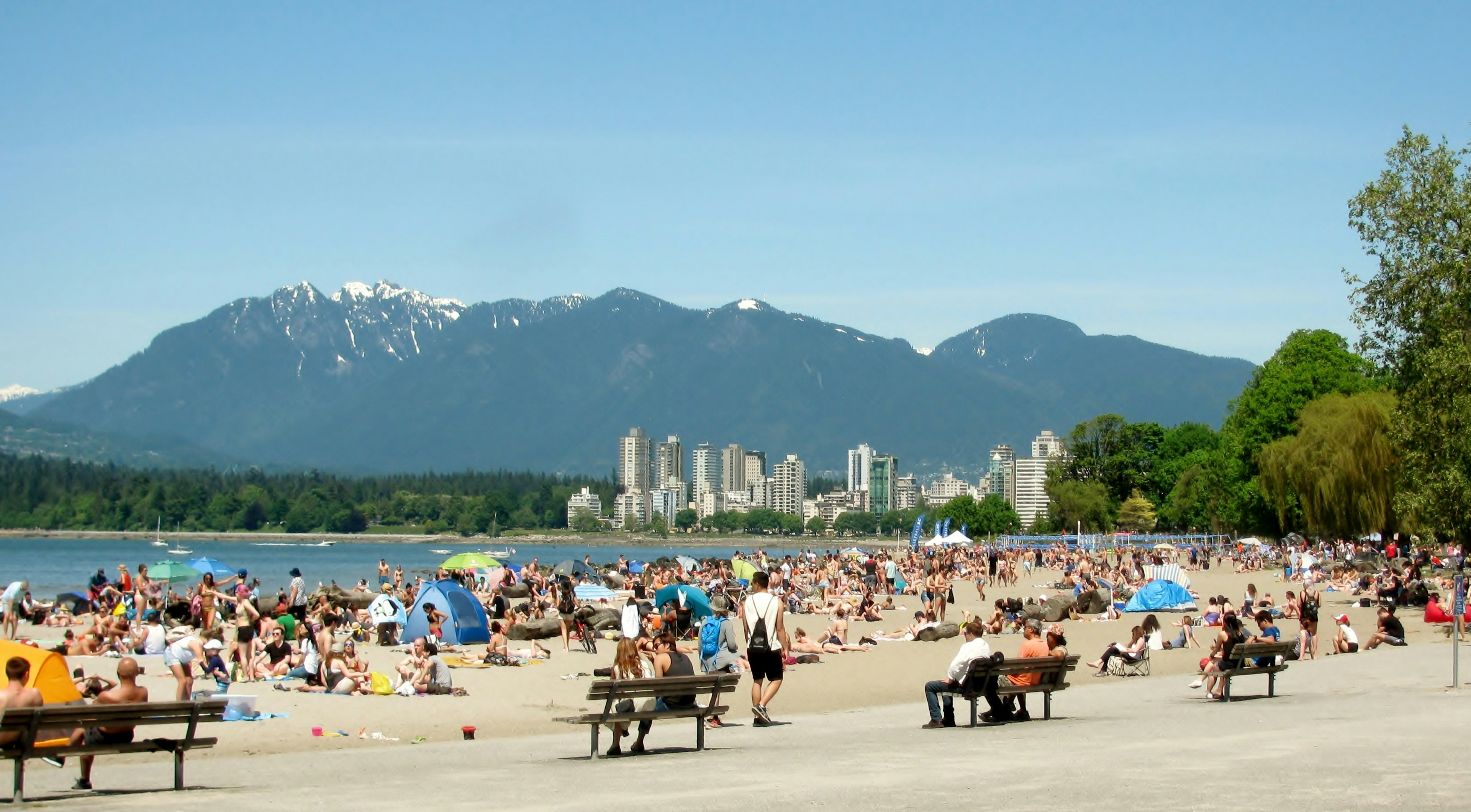 People enjoy a beach on a sunny day with mountains in the background.