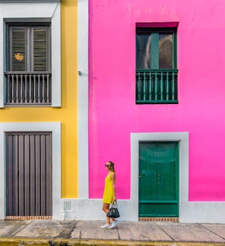 December 12, 2017: Woman in a yellow dress in front of Colourful facades in Old San Juan.