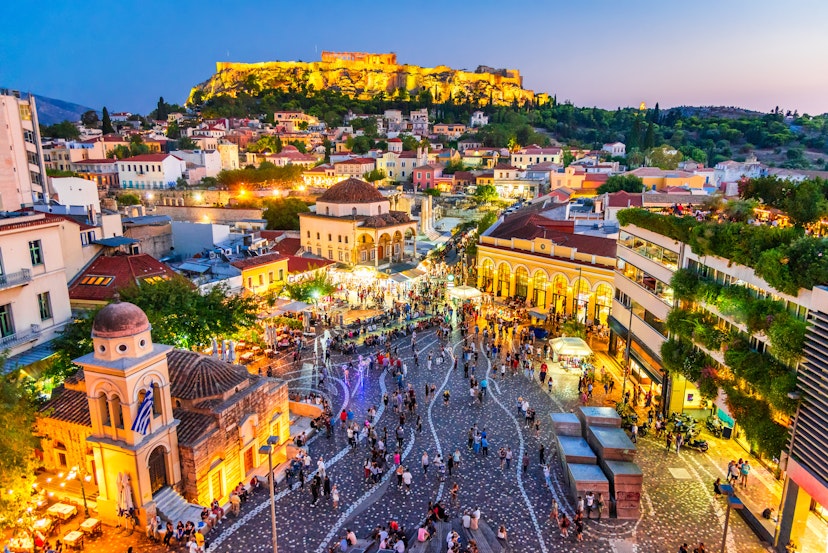 Crowd gathers at Monastiraki Square at night with the ancient Acropolis in the background. 