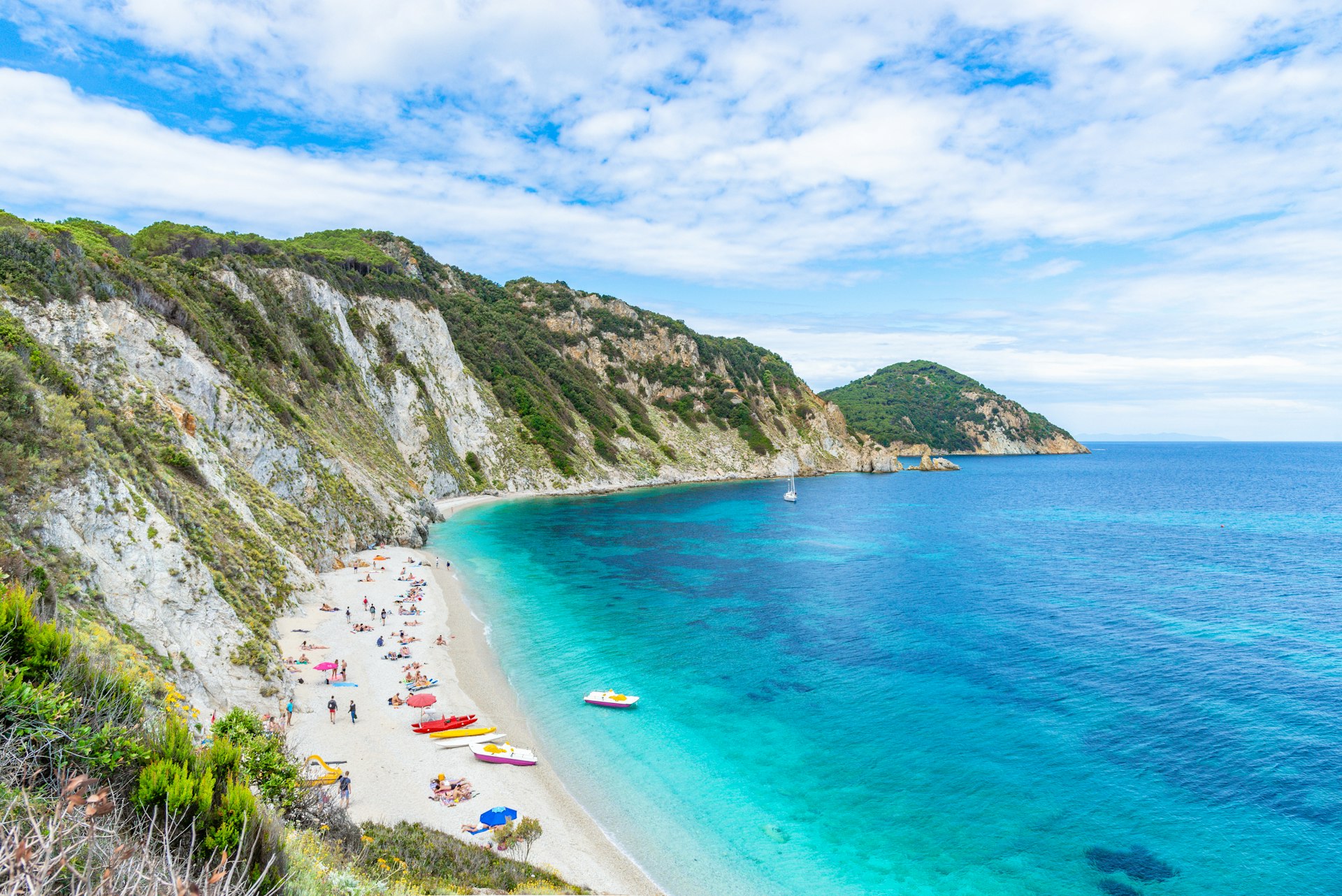 High-angle view of Sansone Beach on Elba Island. The beach has white sand and turquoise waters, and is backed by a large cliff.